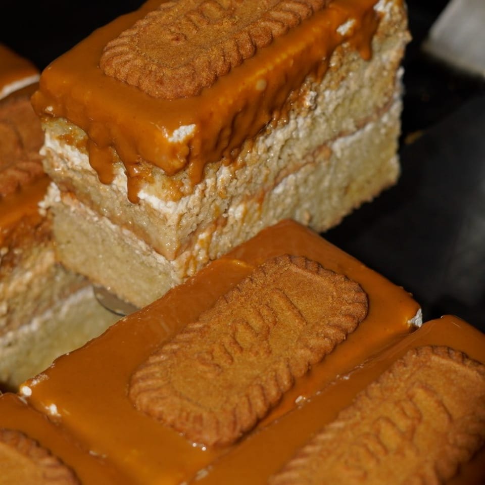 Stacked caramel-glazed layered cakes topped with rectangular cinnamon biscuits on a dark serving surface.