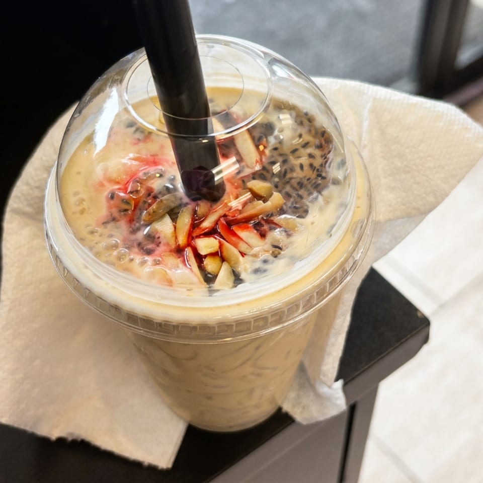 Iced creamy beverage topped with fruit, nuts, and black seeds in a clear cup on a napkin.