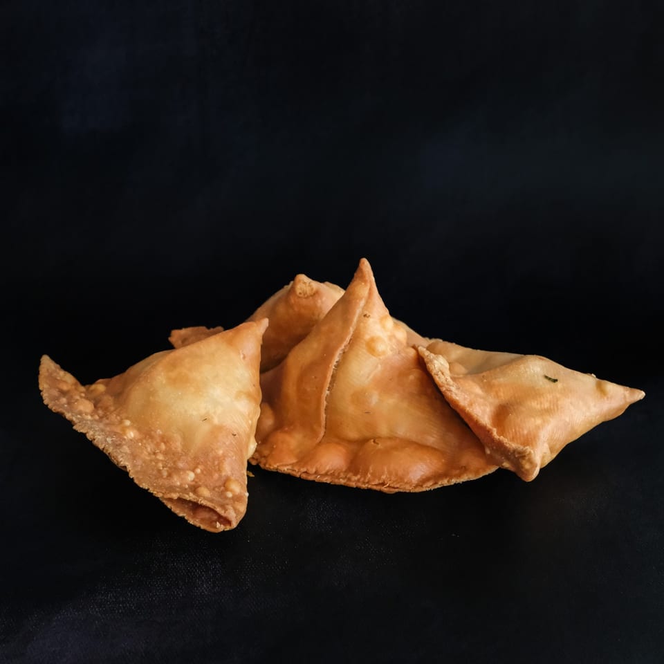 Golden triangular samosas against a dark background.