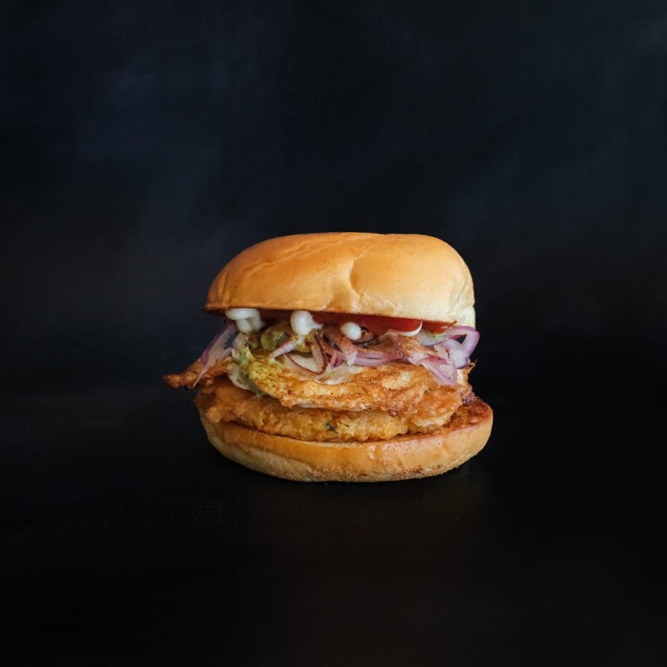 Burger layered with a golden patty, egg, red onion, and sauces.