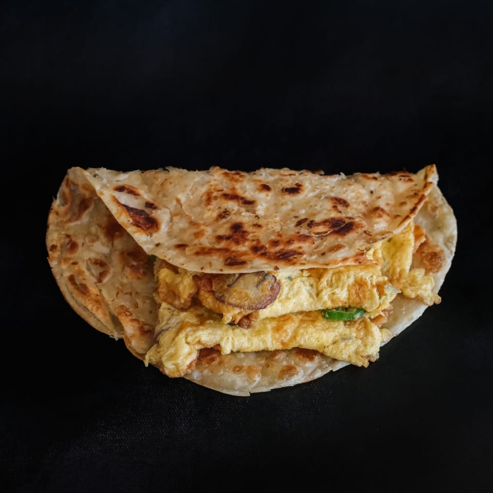 Golden folded paratha with an egg filling against a dark background.